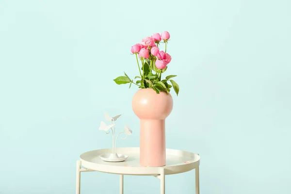 Vase with beautiful peony roses on table against color wall