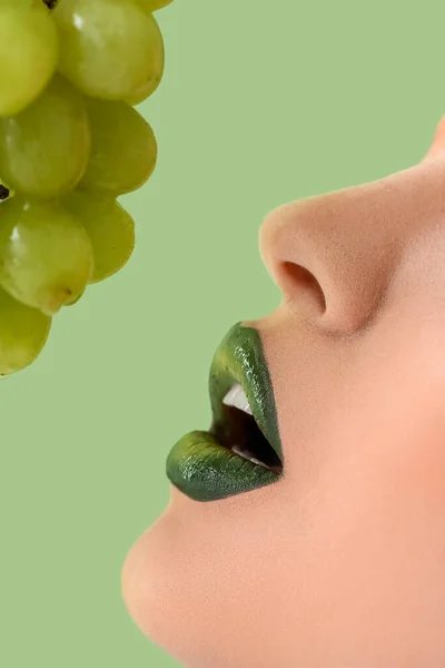 Beautiful young woman with unusual makeup and grapes on color background, closeup