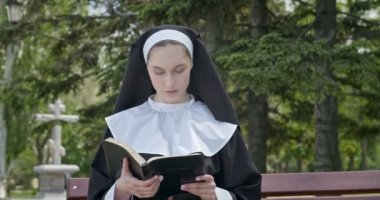 Genç rahibe dışarıda İncil okuyor.