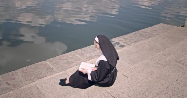 Joven Monja Leyendo Biblia Cerca Del Río — Vídeo de stock