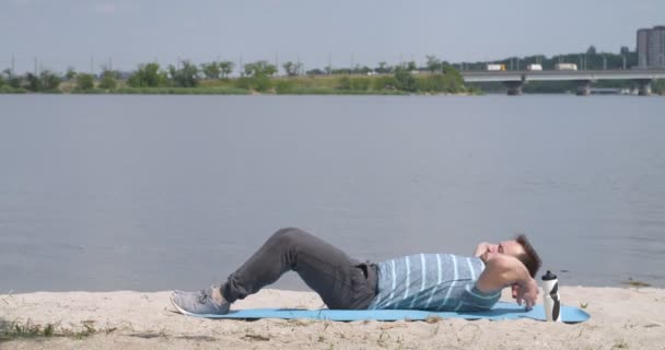 瘦小的年轻人在河边做仰卧起坐 — 图库视频影像