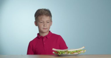 Küçük çocuk arka planda lezzetli sandviçler yiyor.