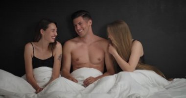 Yakışıklı genç bir adam ve yatakta iki güzel kadın. Poliyamory konsepti
