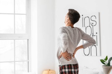 Yatak odasında sırt ağrısı çeken genç bir adam.