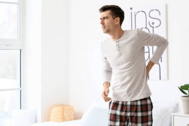 Yatak odasında sırt ağrısı çeken genç bir adam.