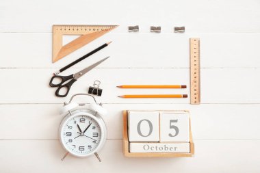 Beyaz ahşap zemin üzerinde küp takvim, alarm saati ve kırtasiye malzemesi