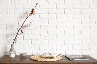 Pamuk çiçekli vazo ve tuğla duvarın yanındaki masada defter.