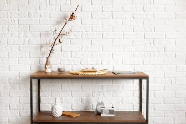 Ağaç dalı ve dekorlu vazo tuğla duvarın yanında.