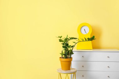Süslü odanın içindeki masada saat ve ev bitkisi var.