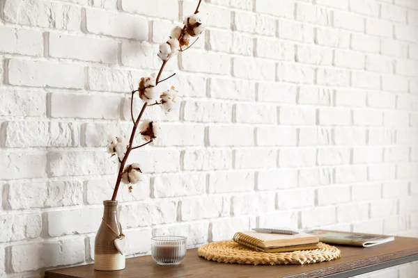 Pamuk çiçekli vazo ve tuğla duvarın yanındaki masada defter.