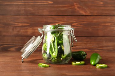 Ahşap arka planda yeşil biberli cam kavanoz.