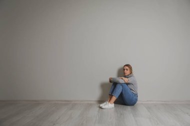 Depresyondaki genç kadın gri duvarın yanında oturuyor.