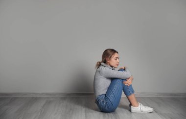 Depresyondaki genç kadın gri duvarın yanında oturuyor.