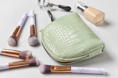 Zarif makyaj çantası, fırçalar, makyaj temeli ve arka planda kirpik kıvırıcı, yakın plan.