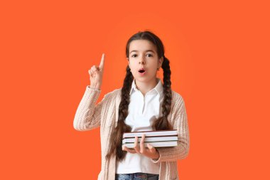 Kitapları olan sevimli küçük bir okul kızı ve renkli arka planda işaret parmağını kaldırdı.