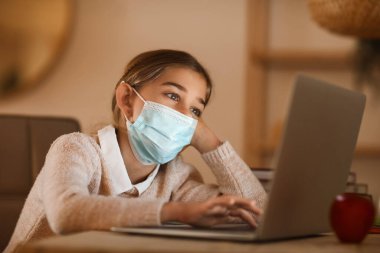 Tıp maskeli küçük kız evde internetten çalışıyor.