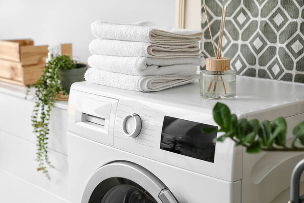 Modern washing machine with towels and reed diffuser in bathroom