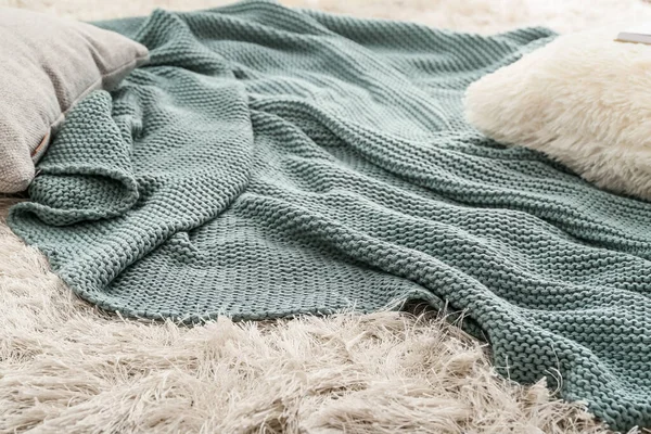 Knitted plaid with pillows on carpet