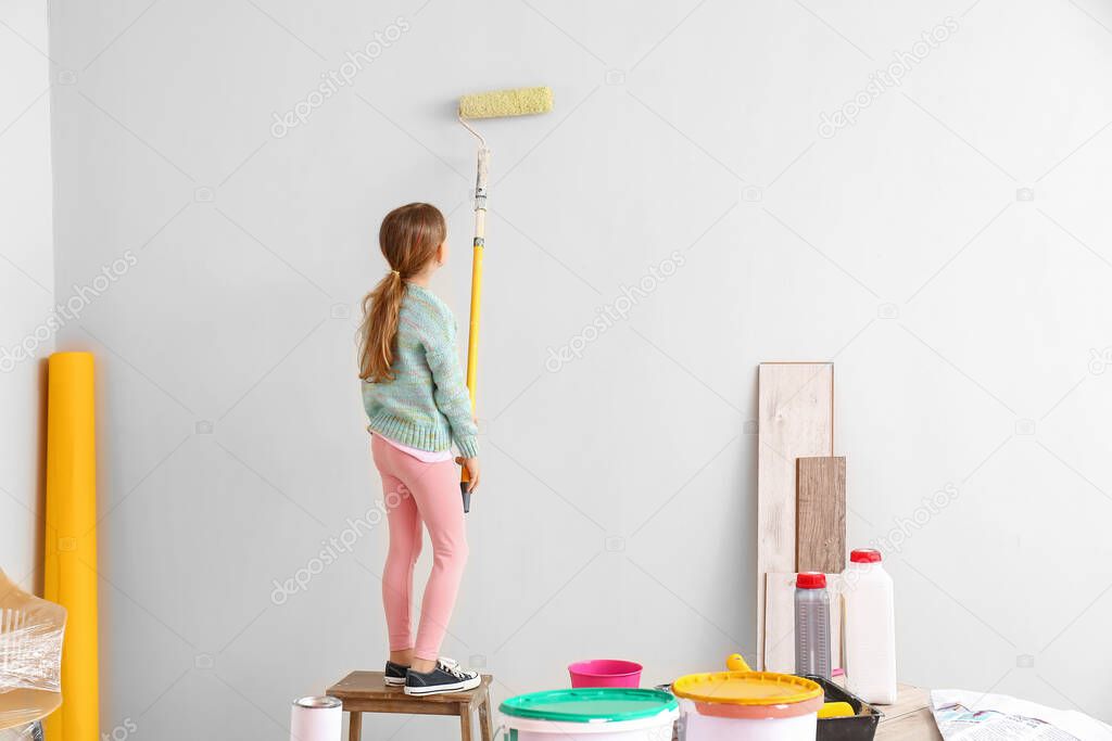 Little girl painting wall in room