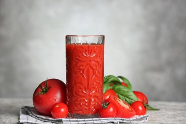 Gri arkaplanda bir bardak lezzetli domates suyu.