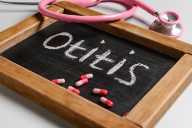 Kelime OTITIS, steteskop ve hafif arka planda haplar içeren tahta