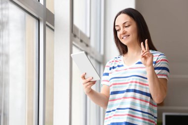 Pencerenin yanında tablet bilgisayarı olan genç bir kadın