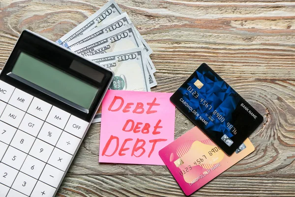 Paper with word DEBT, money and calculator on wooden background