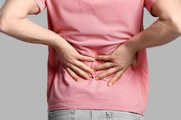 Young man suffering from flank pain on grey background Stock Photo