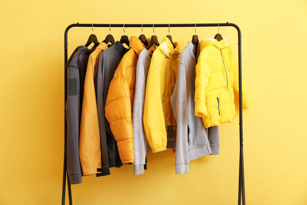 Стойка со стильной одеждой рядом с цветной стеной