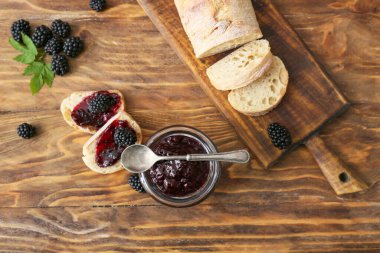 Lezzetli böğürtlen reçeli kavanozu ve ahşap arka planda sandviçler