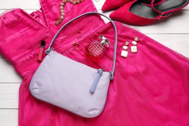 Beyaz ahşap arka planda şık el çantası, elbise ve aksesuarları olan kompozisyon