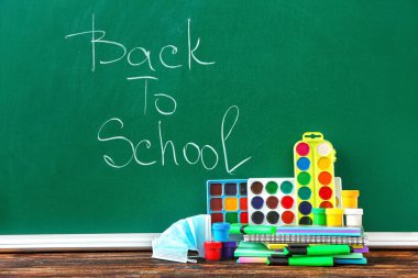 Sınıftaki masadaki kırtasiye ve tıbbi maske setini okula geri gönder.