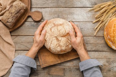 Tahta masada taze ekmeği olan bir erkek fırıncı.