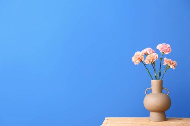 Renk duvarının yanındaki masada karanfil çiçekli vazo.