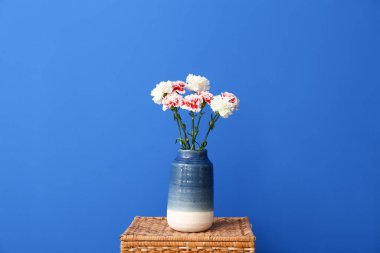 Renkli duvarın yanındaki sepetin üzerinde karanfil çiçekleri olan vazo.