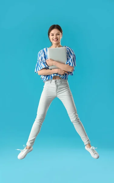 带着彩色背景笔记本电脑跳起来的年轻女子 — 图库照片
