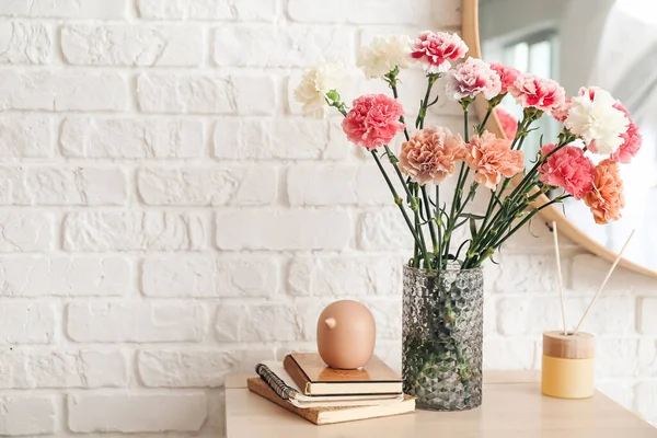 レンガの壁の近くの棚にカーネーションの花 リードディフューザー付き花瓶 — ストック写真