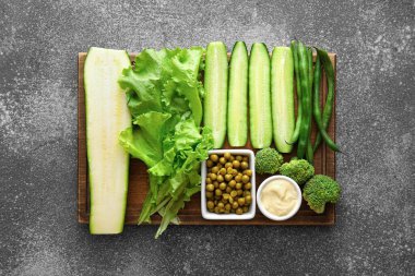 Gri arka planda farklı yeşil sebzeleri olan tahta