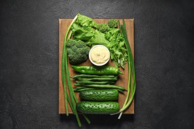 Farklı yeşil sebzeli pano ve koyu arkaplan soslu kase.