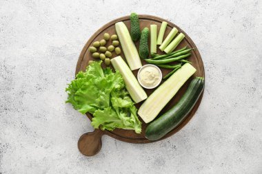 Farklı yeşil sebzeli pano ve açık arkaplan soslu kase.