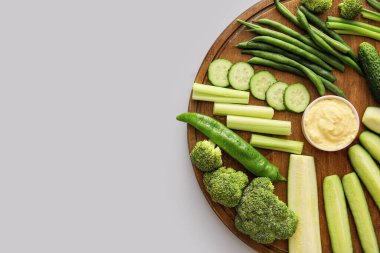 Farklı yeşil sebzeli pano ve açık arkaplan soslu kase.