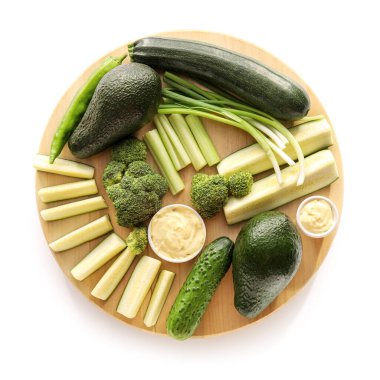 Farklı yeşil sebzeli pano ve beyaz arka planda soslu kase.