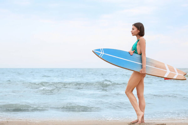 Beautiful young woman with surfboard on beach at resort