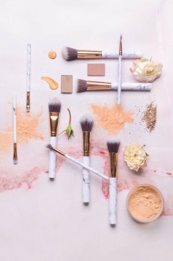 Hafif arkaplanda kozmetik örnekleri bulunan makyaj fırçaları