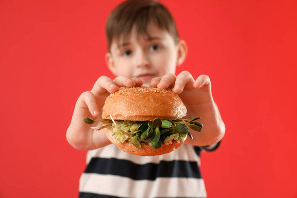 Маленький мальчик с вкусным веганским бургером на цветном фоне, крупным планом