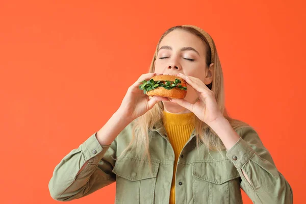 若い女性食べるおいしいビーガンバーガー上の色の背景 — ストック写真