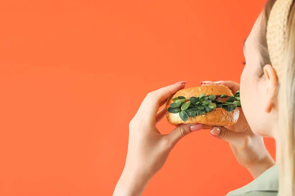 若い女性食べるおいしいビーガンバーガー上の色の背景 — ストック写真