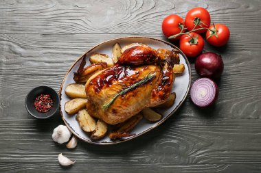 Gri ahşap arka planda fırında tavuk, sebze ve baharat tabağı.