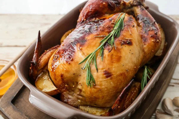 Baking dish with tasty chicken and potato on light wooden background, closeup