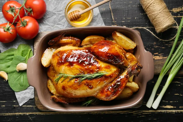 Baking dish with tasty chicken, honey and vegetables on dark wooden background
